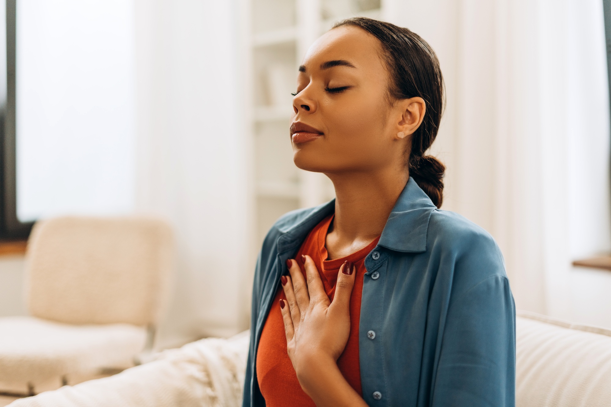 Portrait of beautiful, young African American woman meditating, breathes deeply, relaxing at home